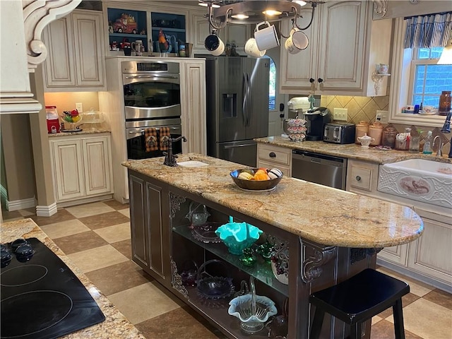 kitchen featuring decorative backsplash, appliances with stainless steel finishes, cream cabinets, open shelves, and a sink