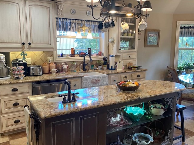 kitchen with cream cabinetry, dishwasher, decorative backsplash, and light stone countertops