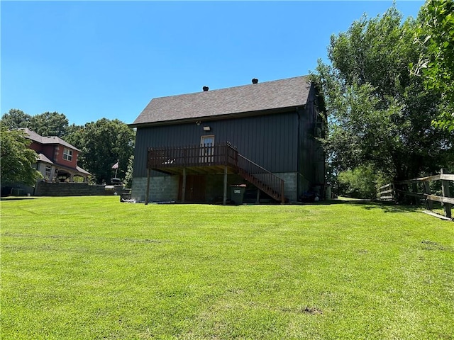 rear view of house with roof with shingles, a lawn, fence, and stairs