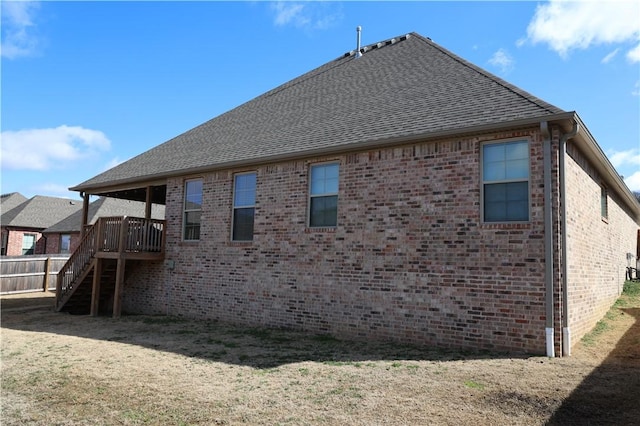 rear view of property featuring stairway, brick siding, and roof with shingles