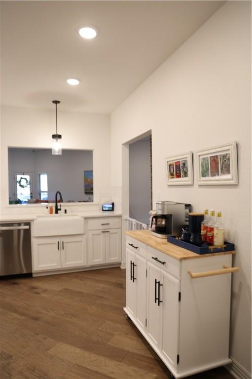 kitchen featuring dark wood-style floors, a sink, hanging light fixtures, white cabinets, and stainless steel dishwasher