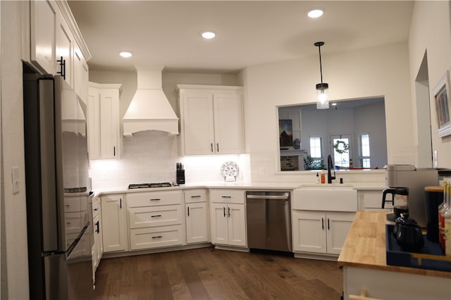 kitchen featuring appliances with stainless steel finishes, custom exhaust hood, white cabinets, wood counters, and a sink