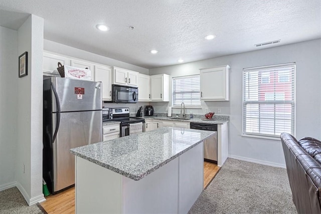 kitchen featuring visible vents, a kitchen island, a sink, appliances with stainless steel finishes, and white cabinetry