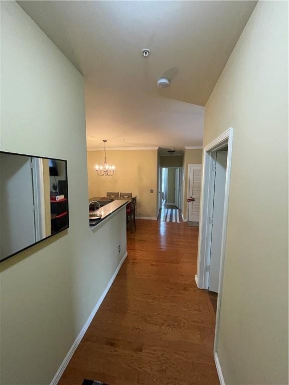 corridor with a notable chandelier, wood finished floors, baseboards, and ornamental molding