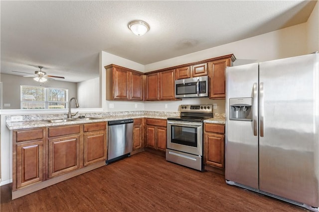 kitchen featuring a sink, light stone counters, dark wood finished floors, appliances with stainless steel finishes, and brown cabinetry