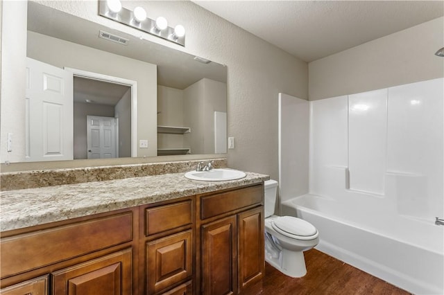 bathroom featuring visible vents, toilet, wood finished floors, vanity, and a textured wall