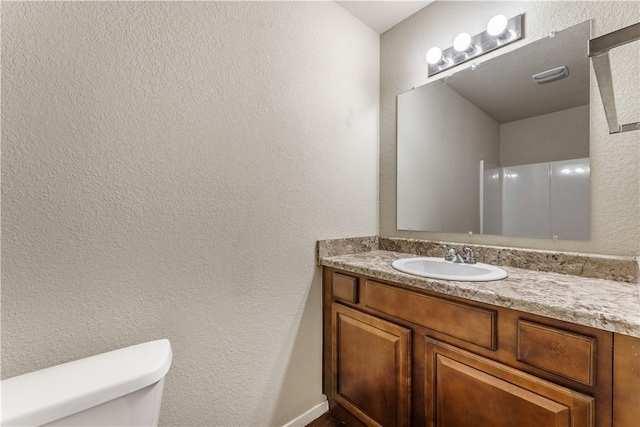 bathroom featuring toilet, vanity, and a textured wall