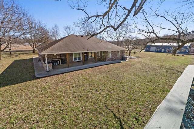 rear view of property featuring a patio, a lawn, and brick siding