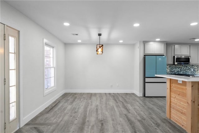 kitchen with visible vents, freestanding refrigerator, light countertops, stainless steel microwave, and tasteful backsplash