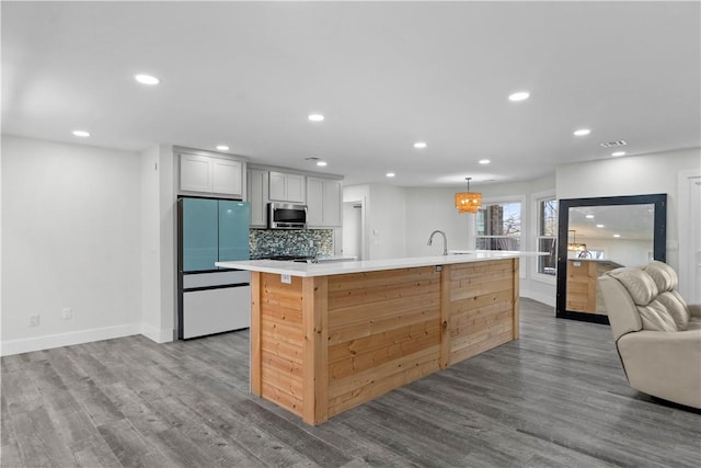 kitchen with stainless steel microwave, light countertops, freestanding refrigerator, and wood finished floors