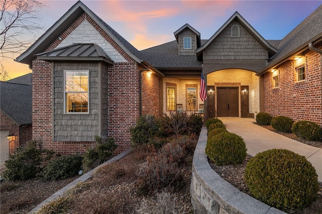 view of front of property featuring brick siding, a shingled roof, concrete driveway, metal roof, and a standing seam roof