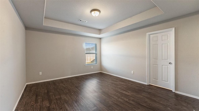 unfurnished room with a tray ceiling, baseboards, visible vents, and dark wood-style flooring