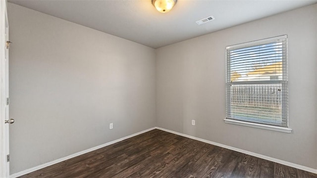 spare room with dark wood finished floors, visible vents, and baseboards