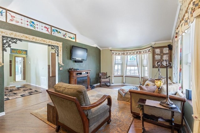 living room featuring visible vents, wood finished floors, a glass covered fireplace, crown molding, and baseboards