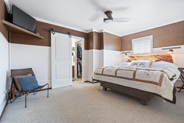 bedroom featuring a wainscoted wall, ornamental molding, a barn door, carpet, and a spacious closet