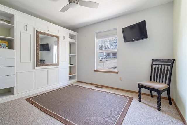 living area featuring visible vents, built in shelves, a ceiling fan, carpet, and baseboards