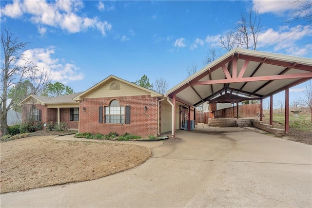 view of front of house featuring brick siding, a detached carport, fence, concrete driveway, and central AC