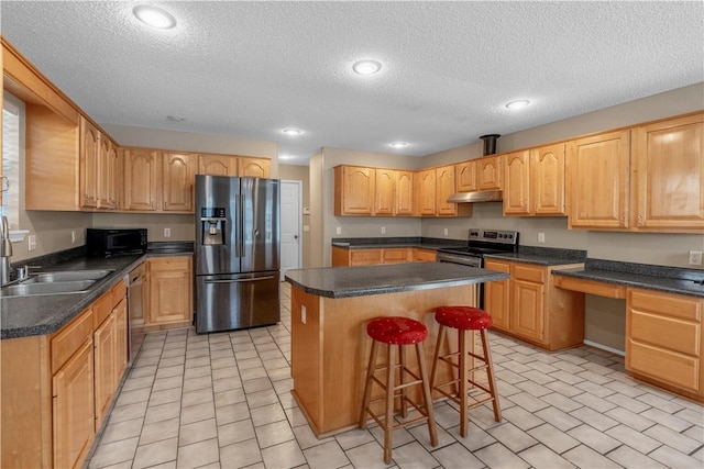 kitchen with under cabinet range hood, a sink, a center island, built in desk, and appliances with stainless steel finishes