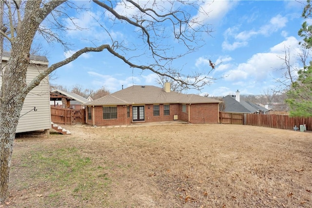 rear view of house featuring brick siding, a lawn, a chimney, and fence