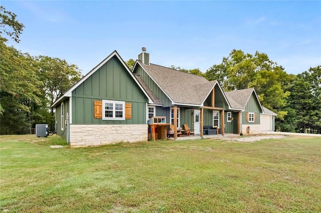 view of front of home with central air condition unit, roof with shingles, board and batten siding, a front yard, and a chimney