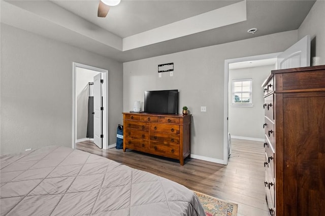 bedroom featuring a ceiling fan, a raised ceiling, baseboards, and wood finished floors