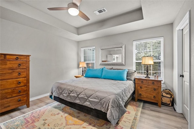 bedroom with a tray ceiling, visible vents, light wood-type flooring, and baseboards