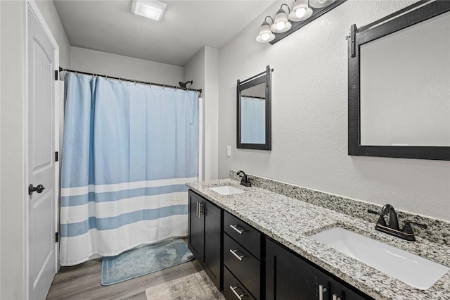 bathroom featuring double vanity, wood finished floors, a shower with shower curtain, and a sink