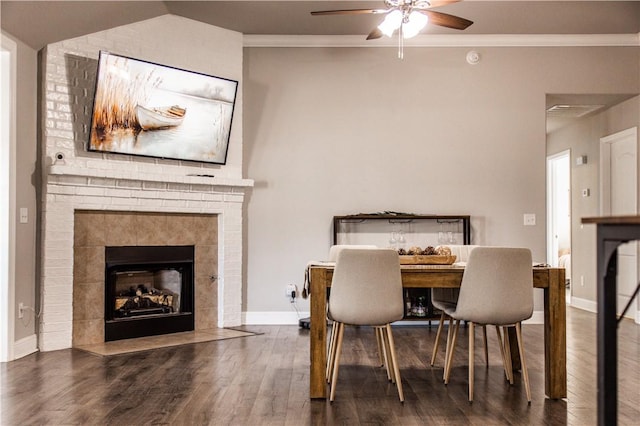 dining room featuring baseboards, a tiled fireplace, ornamental molding, wood finished floors, and a ceiling fan