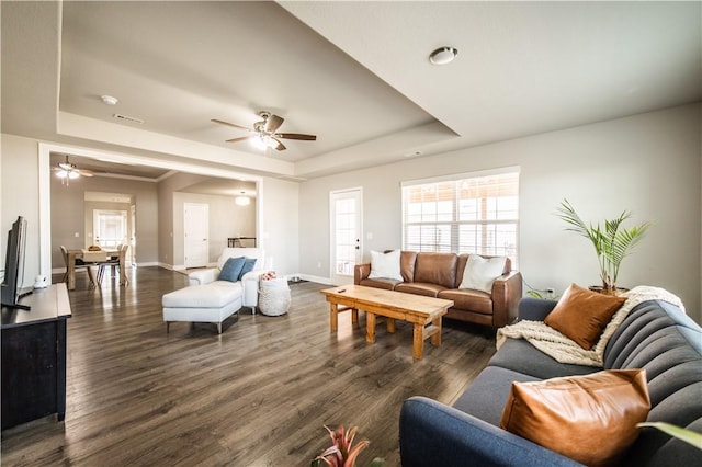 living room featuring a ceiling fan, a tray ceiling, baseboards, and dark wood-type flooring