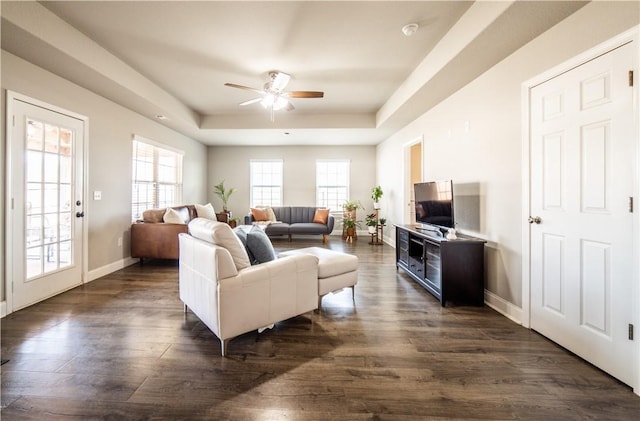 living area featuring a ceiling fan, a raised ceiling, baseboards, and dark wood-type flooring