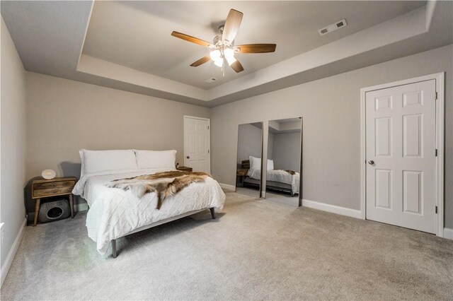 bedroom with visible vents, light carpet, a raised ceiling, baseboards, and ceiling fan