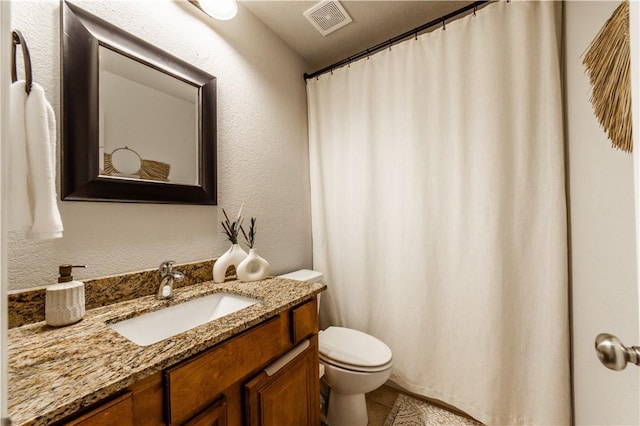 bathroom with tile patterned floors, visible vents, toilet, vanity, and a textured wall