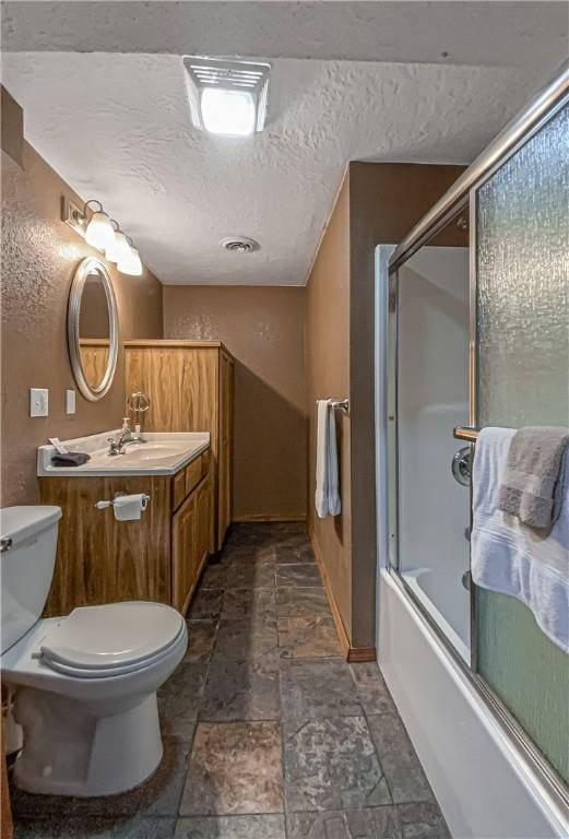 full bath with toilet, stone finish floor, a textured ceiling, enclosed tub / shower combo, and vanity