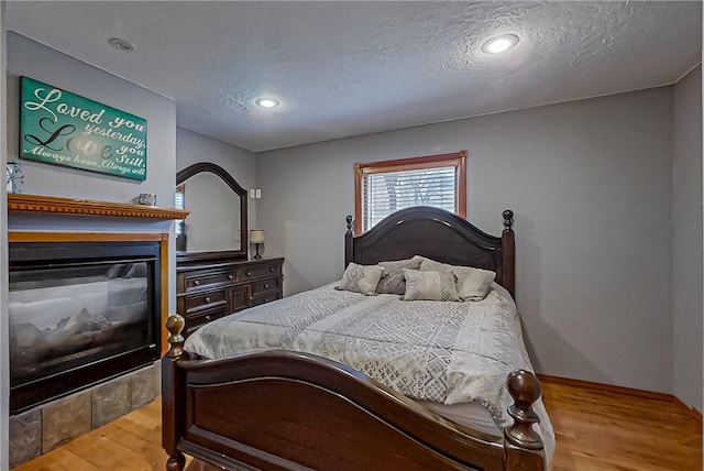 bedroom with recessed lighting, wood finished floors, a multi sided fireplace, and a textured ceiling