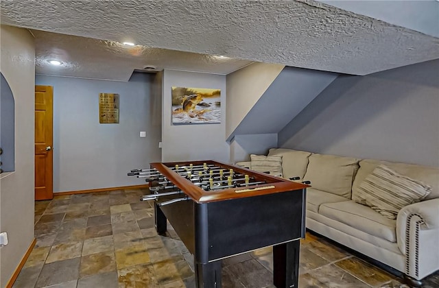 rec room with stone finish floor, a textured ceiling, and baseboards