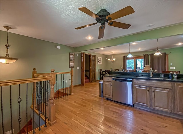 kitchen featuring a sink, stainless steel dishwasher, dark countertops, and light wood-style flooring