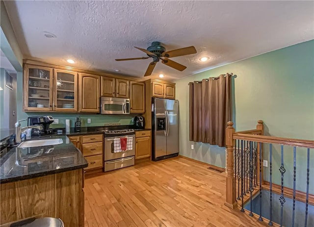 kitchen with a sink, glass insert cabinets, light wood-style floors, appliances with stainless steel finishes, and a textured ceiling