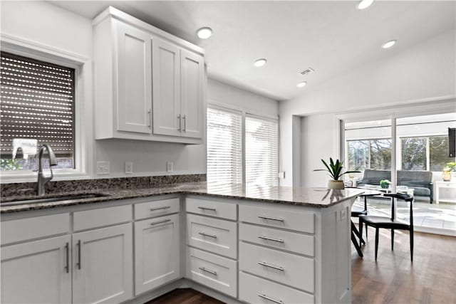 kitchen with vaulted ceiling, recessed lighting, dark stone countertops, a peninsula, and a sink