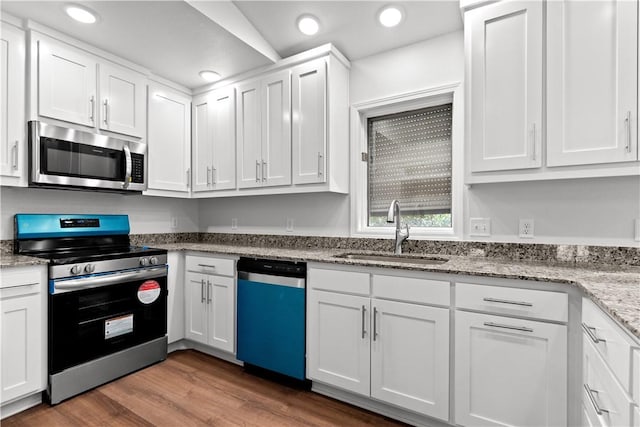 kitchen with a sink, stainless steel appliances, wood finished floors, and white cabinets