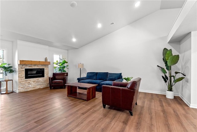 living area with a stone fireplace, a healthy amount of sunlight, lofted ceiling, and wood finished floors