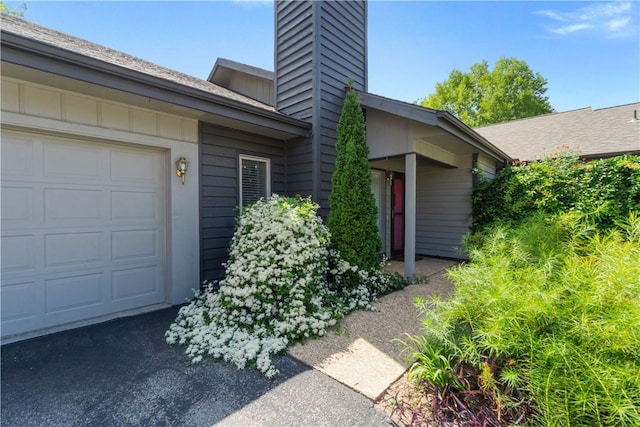 doorway to property with aphalt driveway, board and batten siding, a chimney, and a garage