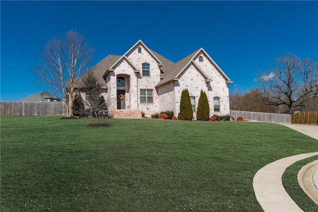 french country inspired facade featuring brick siding, a front yard, and fence