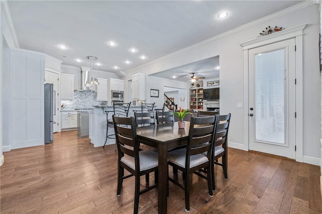 dining room featuring hardwood / wood-style floors, recessed lighting, a fireplace, crown molding, and ceiling fan