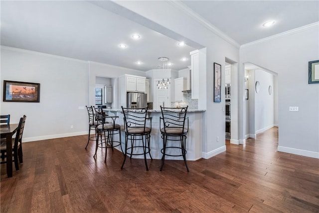 kitchen with backsplash, dark wood-type flooring, a kitchen bar, white cabinets, and stainless steel appliances