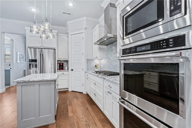 kitchen with appliances with stainless steel finishes, white cabinetry, wall chimney range hood, and ornamental molding