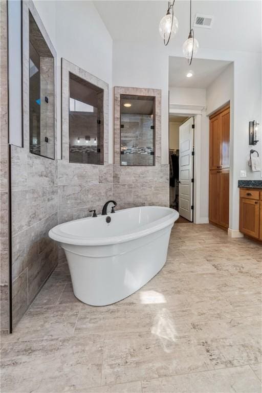 full bathroom with visible vents, a freestanding bath, vanity, tiled shower, and tile walls