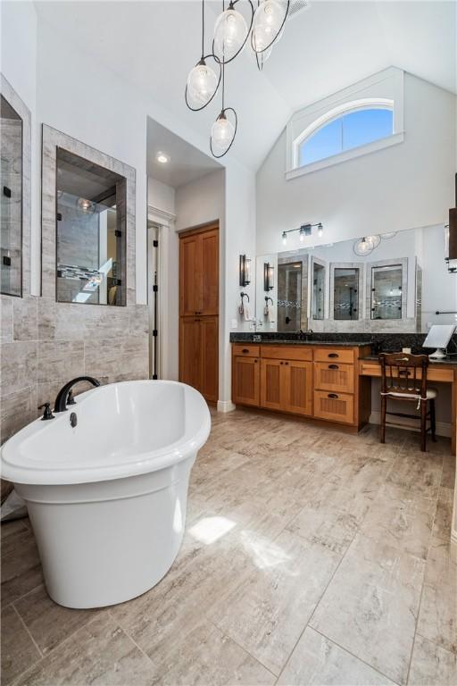 full bathroom featuring high vaulted ceiling, tile walls, tiled shower, a freestanding bath, and vanity