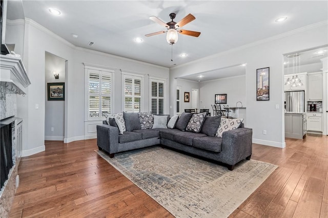 living room with light wood-type flooring, ornamental molding, a ceiling fan, a fireplace, and baseboards