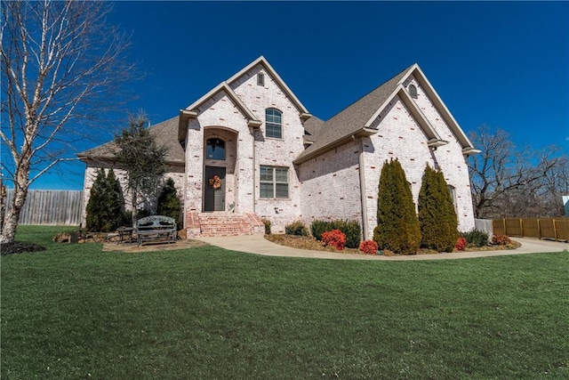 french provincial home with brick siding, a shingled roof, a front lawn, and fence