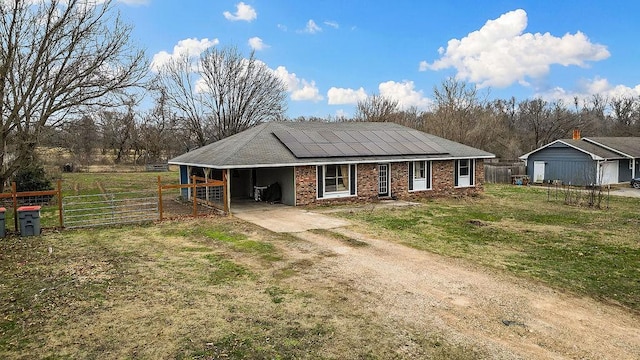 view of front facade with an attached carport, a front lawn, dirt driveway, brick siding, and roof mounted solar panels